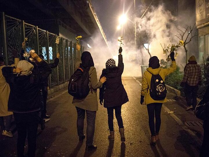 Demonstrantinnen erinnern mit weißen Blumen an die Opfer des Flugzeugabschusses, während Sicherheitskräfte Tränengas in ihre Richtung schießen.