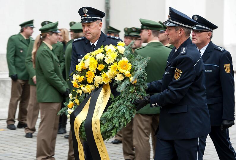 Polizisten der Landespolizei Baden-Württemberg tragen einen Trauerkranz für den ermordeten Polizisten aus Augsburg.