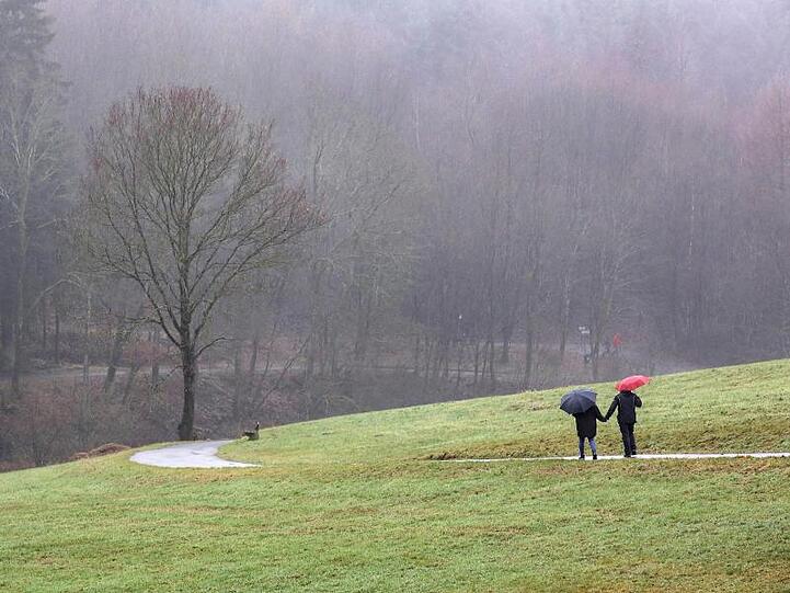 Spaziergänger sind mit Regenschirmen an einem nebligen tristen Wintertag unterwegs.