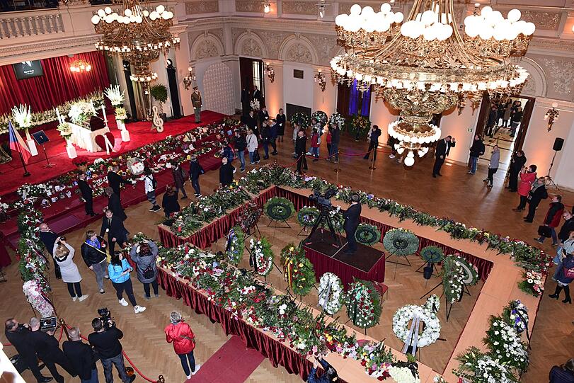Menschen gehen durch einen Raum im Prager Sophienpalais, in dem der Sarg mit dem Leichnam des Sängers Karel Gott aufgebahrt ist, und legen Blumen und Botschaften nieder.