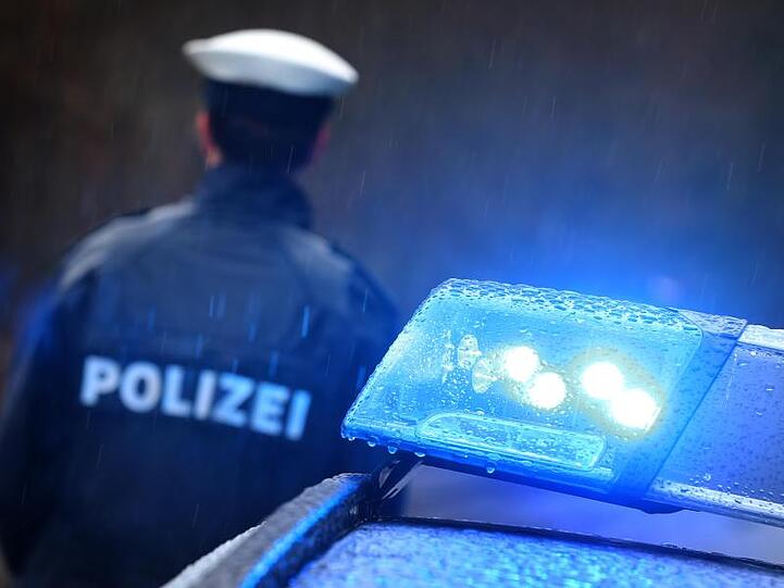 Ein Polizist steht im Regen vor einem Streifenwagen dessen Blaulicht aktiviert ist. Foto: Karl-Josef Hildenbrand/dpa