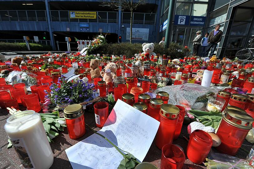 Tiefe Trauer: Passanten betrachten die Kuscheltiere, Grußkarten und Kerzen, die zum Gedenken an das elfjährige Mädchen, dass am Samstag im City-Parkhaus am Wasserturm in Emden ermordet wurde, vor der Einfahrt zum Parkhaus liegen.