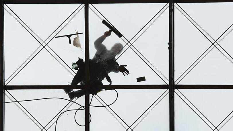 Zwei Gebäudereiniger putzen in Dresden das gewölbte Glasdach des World Trade Centers.