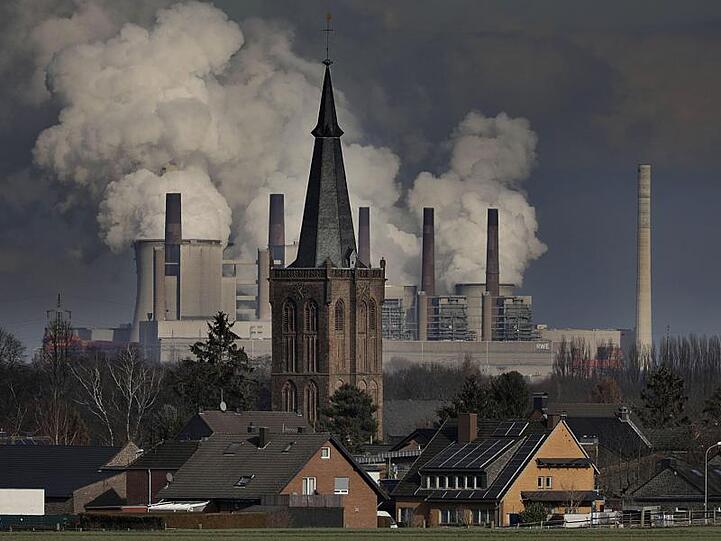 Rauch und Dampf steigen aus dem RWE Braunkohlekraftwerk Neurath hinter der St. Martinus Kirche im Ortsteil Niederembt auf.