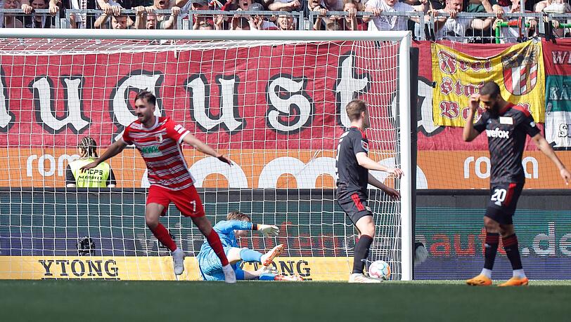 Augsburgs Dion Drena Beljo (l) jubelt nach seinem Tor zum 1:0, der Berliner Torwart Frederik Rönnow (M) schaut dem Ball im Netz nach.