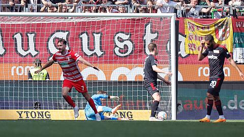 Augsburgs Dion Drena Beljo (l) jubelt nach seinem Tor zum 1:0, der Berliner Torwart Frederik Rönnow (M) schaut dem Ball im Netz nach.