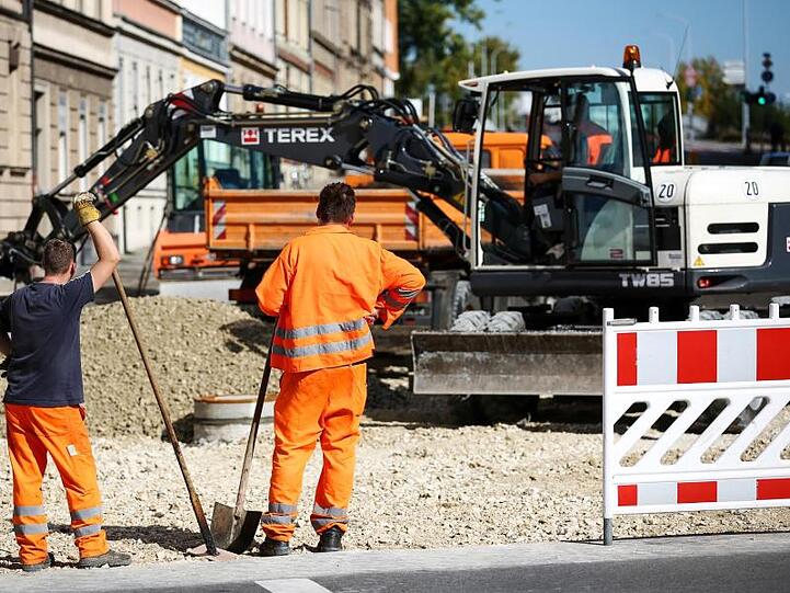 Zwei Bauarbeiter schauen beim Verteilen von Kies an einer Baustelle zu. Foto: David-Wolfgang Ebener/Archiv