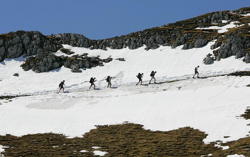 Eine Gruppe Wanderer geht oberhalb der Bergstation der Karwendelbahn bei Mittenwald (Bayern) auf über 2300 Metern Höhe über ein Schneefeld (Archivbild).