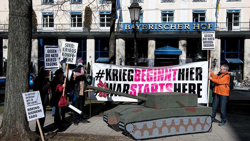 Demonstranten stehen bei einer früheren Demonstration mit Plakaten und einem Papp-Panzer vor dem Bayerischen Hof, in dem die Sicherheitskonferenz stattfindet.