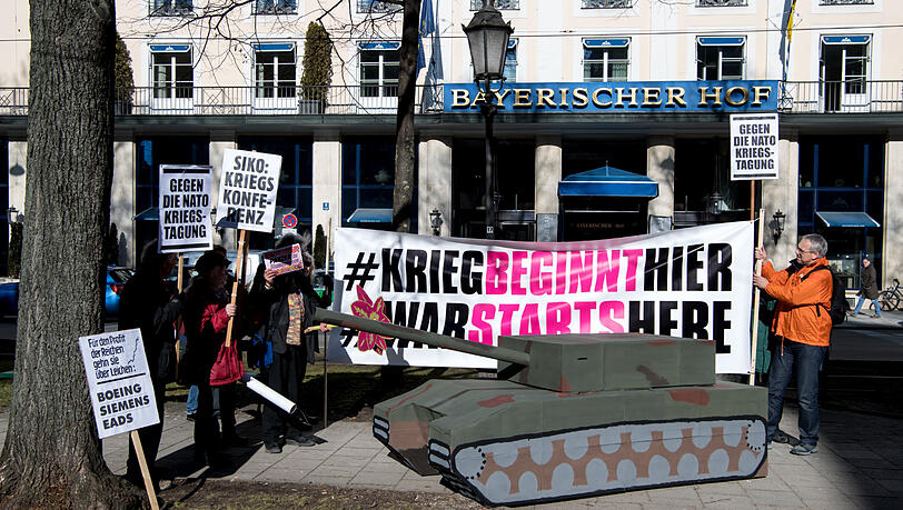 Demonstranten stehen bei einer früheren Demonstration mit Plakaten und einem Papp-Panzer vor dem Bayerischen Hof, in dem die Sicherheitskonferenz stattfindet.
