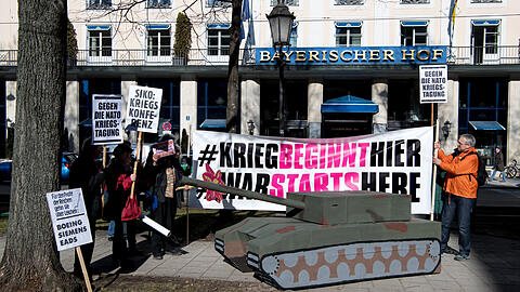 Demonstranten stehen bei einer früheren Demonstration mit Plakaten und einem Papp-Panzer vor dem Bayerischen Hof, in dem die Sicherheitskonferenz stattfindet.
