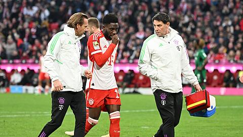 Münchens Alphonso Davies (M) wird von Mannschaftsarzt Peter Ueblacker (l) vom Platz begleitet. Er ist zurück im Lauftraining.