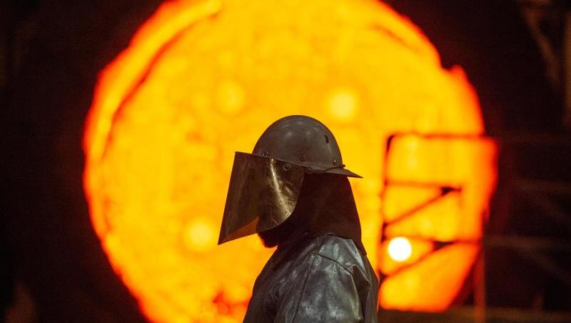 Ein Mitarbeiter steht im Stahlwerk vor einer glühenden Roheisenpfanne. Foto: Christophe Gateau/dpa/Archivbild