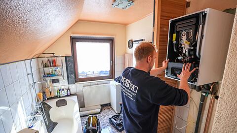 Ein Mitarbeiter einer Sanitär- und Heizungsbaufirma installiert eine moderne Gasbrennwerttherme in einem Einfamilienhaus.