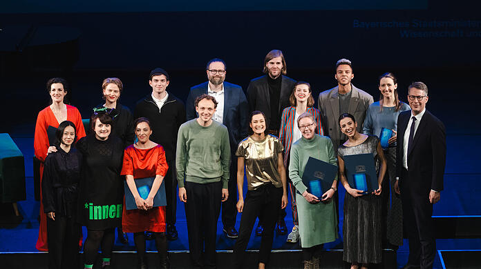 Gruppenfoto mit gegendertem Kleid. Die Preisträgerinnen und Preisträger mit Kunstminister Markus Blume (rechts).