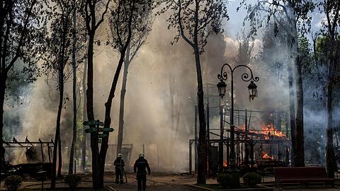 Feuerwehrleute löschen einen Brand, nachdem das russische Militär einen Park in Charkiw bombardiert hat.