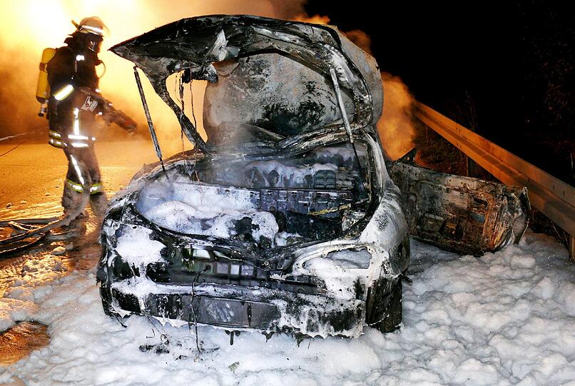 Ein Feuerwehrmann steht am 24.11.2013 neben einem ausgebrannten Autowrack auf der Autobahn A7 bei Hildesheim (Niedersachsen)