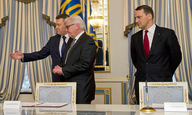 Der ukrainische Staatspräsident Viktor Janukowitsch (links),  Bundesaußenminister Frank-Walter Steinmeier (SPD) und der polnische Außenminister Radoslaw Sikorski stehen an einem Tisch im Präsidentenpalast in Kiew, auf dem Unterschriftenmappen bereit liegen.