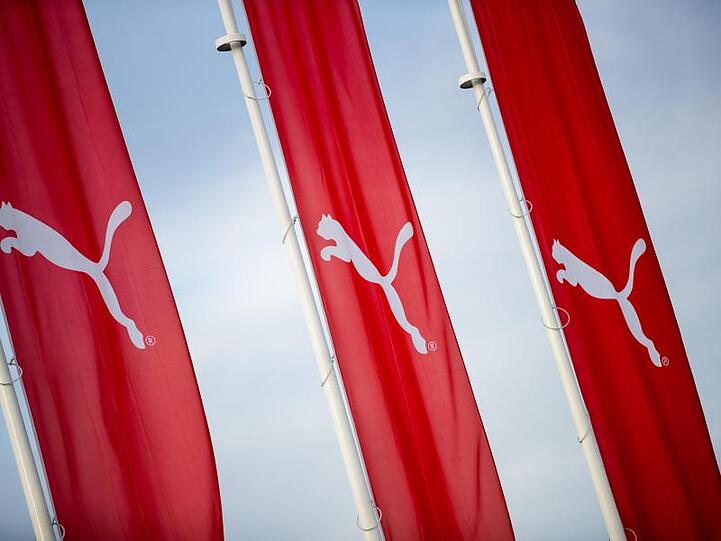 Fahnen mit dem Logo des Sportartikelherstellers Puma SE hängen vor dem Hauptsitz des Unternehmens. Foto: Daniel Karmann