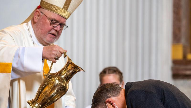 Kardinal Reinhard Marx gießt Weihwasser über den Kopf eines Taufbewerbers. Foto: Lino Mirgeler/dpa
