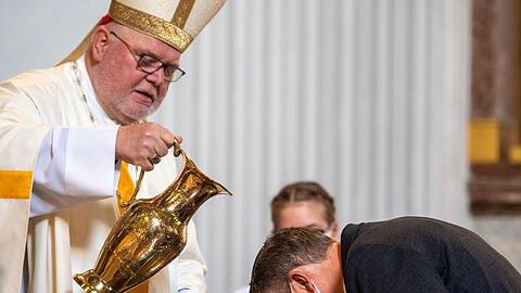 Kardinal Reinhard Marx gießt Weihwasser über den Kopf eines Taufbewerbers. Foto: Lino Mirgeler/dpa