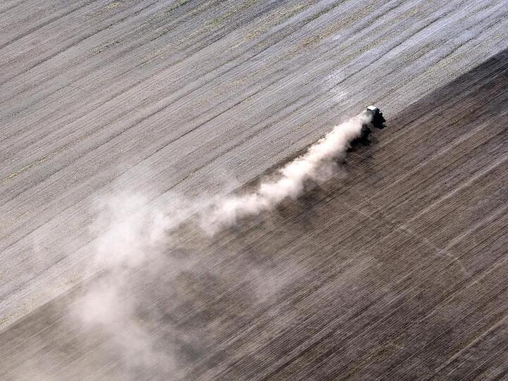 Eine dichte Staubwolke zieht ein Traktor bei Feldarbeiten hinter sich her. Foto: Ralf Hirschberger/Archiv