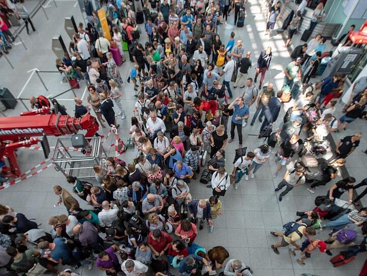 Fluggäste stehen in einem Terminal unter einer Anzeigetafel, auf der viele Flüge als gestrichen angezeigt sind. Foto: Peter Kneffel