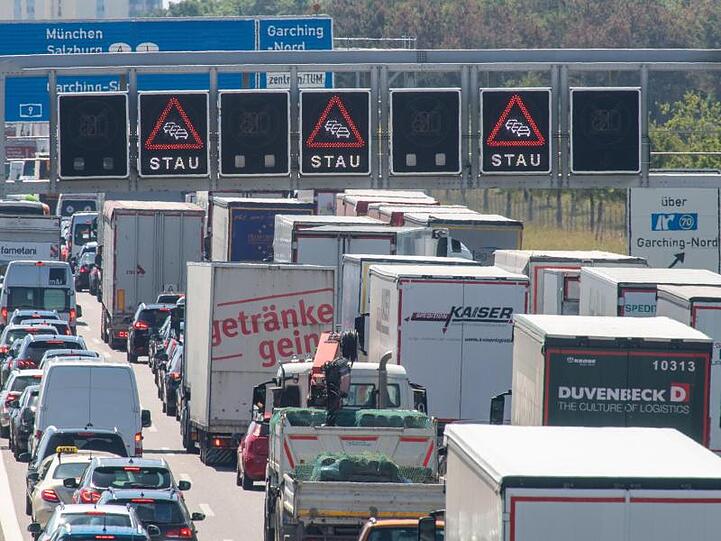 Autos und viele Lastwagen stehen dicht an dicht auf der Autobahn A9 bei München in Fahrtrichtung Süden, während auf Anzeigetafeln Stauwarnungen aufleuchten.