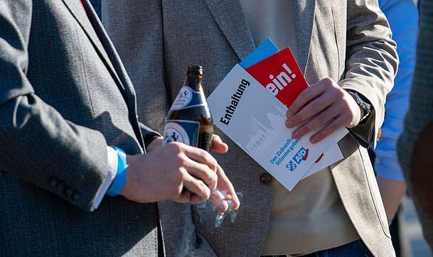 AfD-Anhänger stehen mit Stimmkarten und einer Bierflasche zusammen. AfD-Anhänger stehen mit Stimmkarten und einer Bierflasche zusammen.