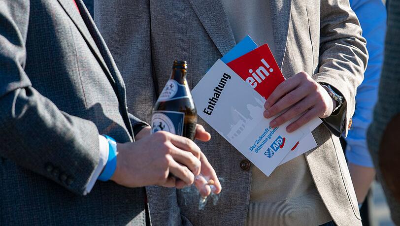 AfD-Anh&auml;nger stehen mit Stimmkarten und einer Bierflasche zusammen.