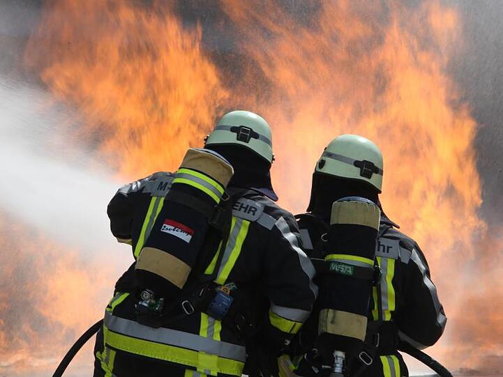 Zwei Feuerwehrmänner löschen unter schwerem Atemschutz das Feuer an einer Simulationsanlage. Foto: Stephan Jansen/Archiv