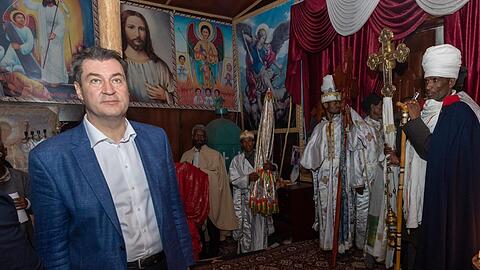 Im Inneren der Wellblechkirche herrscht Zwielicht. Umgeben von Würdenträgern betrachtet Söder die Heiligenbilder.