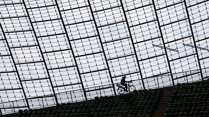 Ein Mitarbeiter des Olympiastadions fährt mit einem Fahrrad am Glasdach der Spielstätte vorbei.