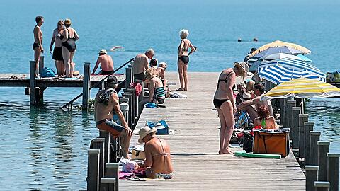 Zahlreiche Ausflügler sitzen bei Sonnenschein und hohen Temperaturen auf einem Steg am Wörthsee. Da können die Parkplätze der umliegenden Gemeinden gerne mal überquellen.