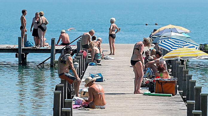 Zahlreiche Ausflügler sitzen bei Sonnenschein und hohen Temperaturen auf einem Steg am Wörthsee. Da können die Parkplätze der umliegenden Gemeinden gerne mal überquellen.