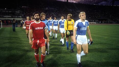 Der FC Bayern und der TSV 1860, angef&uuml;hrt von Gerd M&uuml;ller (l.) und Alfred Kohlh&auml;ufl (r.) beim Einmarsch zum denkw&uuml;rdigen Derby am 12. November 1977 im Olympiastadion vor 77.573 Zuschauern. Hinter M&uuml;ller: FCB-Torwart Sepp Maier.