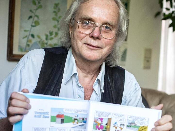 Jan Gulbransson sitzt mit einem Sammelband seiner Comics in seiner Wohnung in München. Foto: Sina Schuldt
