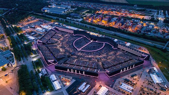 Das volle, extra für Adele aufgestellte Stadion auf dem Freigelände der Messe in Riem. Unmittelbar daneben: Eine temporäre Unterkunft für Geflüchtete.