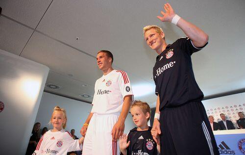Lukas Podolski präsentiert das weiße Champions-League-Trikot der Bayern, Bastian Schweisnteiger kommt im dunkelblauen Auswärts-Jersey daher.