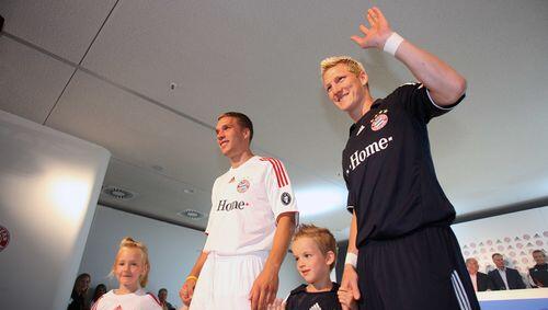 Lukas Podolski präsentiert das weiße Champions-League-Trikot der Bayern, Bastian Schweisnteiger kommt im dunkelblauen Auswärts-Jersey daher. Lukas Podolski präsentiert das weiße Champions-League-Trikot der Bayern, Bastian Schweisnteiger kommt im dunkelblauen Auswärts-Jersey daher.