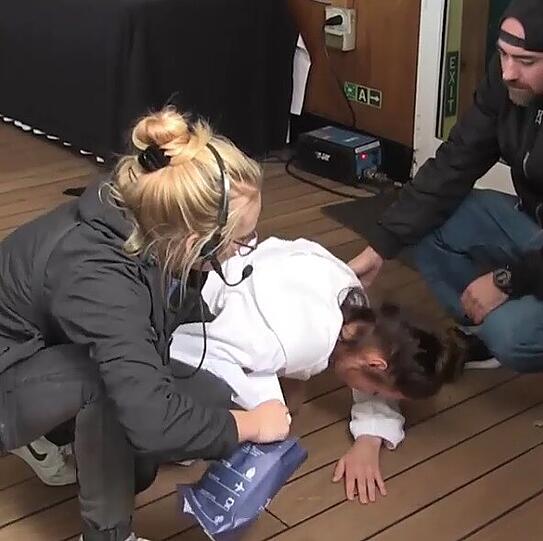 Model Giuliana liegt am Boden, während ein Crew-Mitglied eine Spucktüte bereit hält