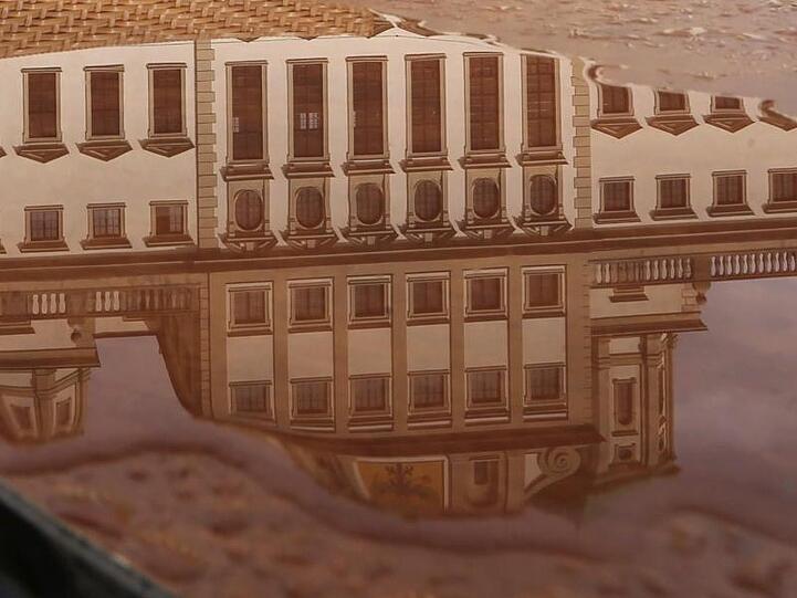Das Augsburger Rathaus spiegelt sich auf dem regennassen Tisch eines Cafés. Foto: Karl-Josef Hildenbrand/dpa/Archivbild