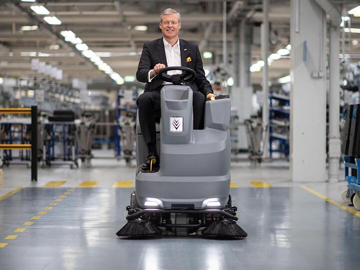 Hartmut Jenner, Vorsitzender des Vorstands der Alfred Kärcher SE & Co. KG, in einer Werkshalle auf einer Scheuersaugmaschine.