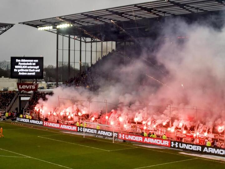 Fans brennen beim Derby zwischen dem FC St. Pauli und dem Hamburger SV Pyrotechnik ab, während eine Anzeigetafel genau davor warnt.