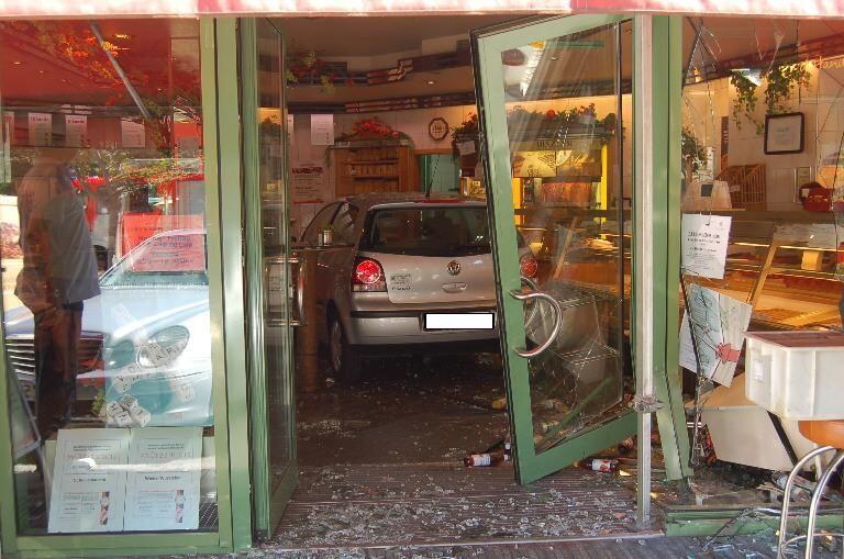 Das Auto der 69-jaehrigen Unfallverursacherin steht am Montag (20.08.12) in Graefeling im scherbenuebersaeten Verkaufsbereich eine Baeckerei, waehrend Verkaeuferinnen der angeschlossenen Metzgerei am Kundentisch stehen