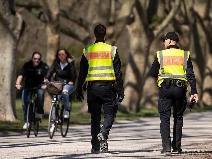 Mitarbeiter des Ordnungsamts kontrollieren in einem Park die Einhaltung der Schutzmaßnahmen. Foto: Marius Becker/dpa/Archivbild