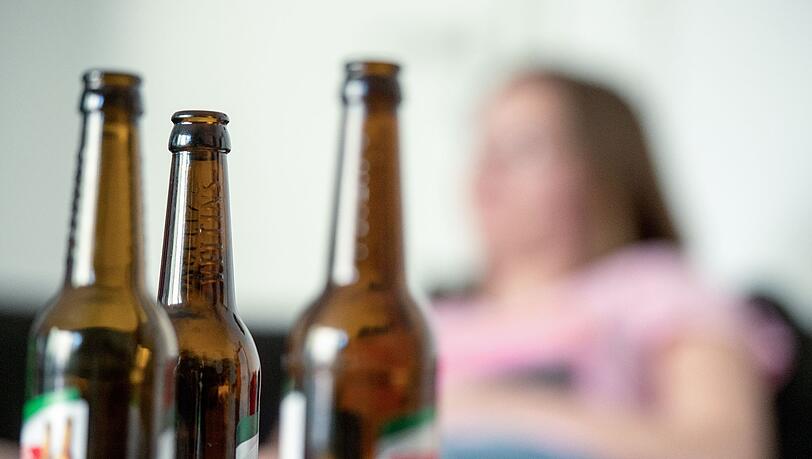 Eine Frau hinter leeren Bierflaschen. Oft ist man direkt vom Alkoholismus des Partners betroffen. (Symbolbild)