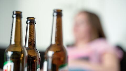 Eine Frau hinter leeren Bierflaschen. Oft ist man direkt vom Alkoholismus des Partners betroffen. (Symbolbild)