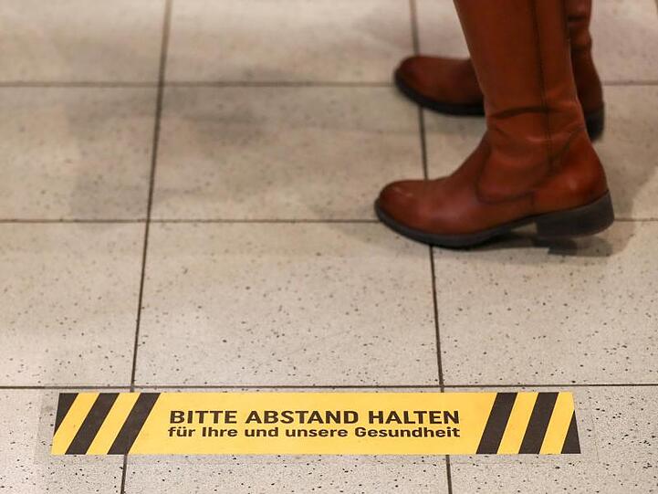 Eine Frau steht an der Kasse eines Supermarkt hinter einem Warnaufkleber, der um Abstand bitte.