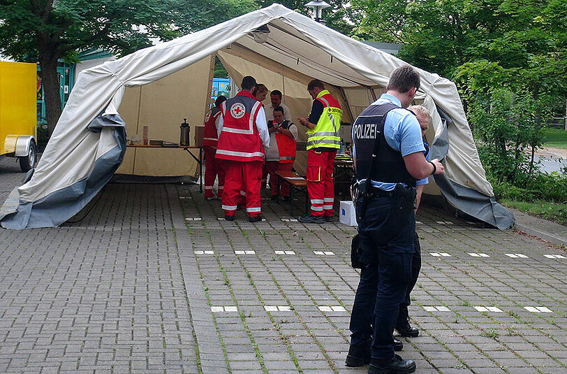 Polizisten stehen am 19.07.2015 in Halberstadt (Sachsen-Anhalt) vor einem Rot-Kreuz-Zelt, das neben einer Sporthalle steht, in der Asylsuchende untergebracht sind. Zuvor waren Helfer des Deutschen-Roten-Kreuzes von Jugendlichen, die "Ausländer raus" skandierten, mit Steinen beworfen worden.